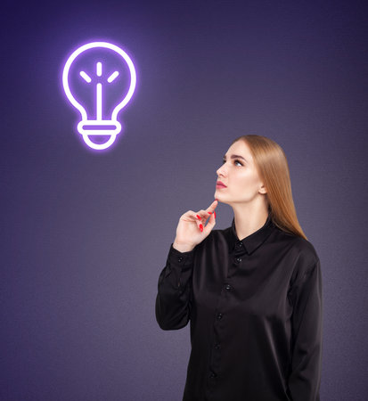 Young woman in black shirt with glowing bulb over head. Over dark blue background.の写真素材