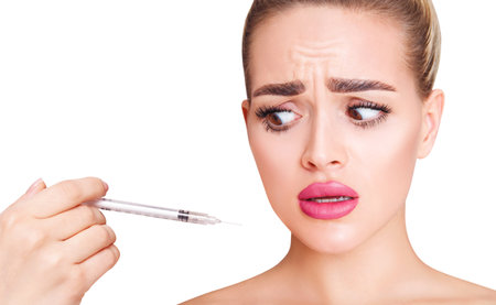 Woman with doubt face looks on syringe. Anti-wrinkles injection concept.の写真素材