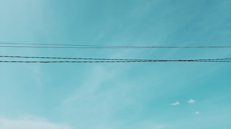 Electrical power lines against a soft turquoise blue sky with wispy cloudsの写真素材
