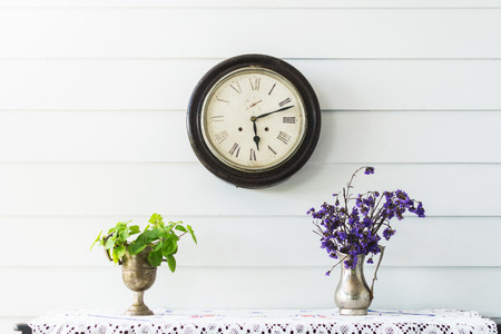 Retro home decor. Flowers and a vintage clock on a white wall shelf.