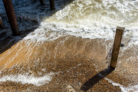 Waves crashing on the beach with old wooden pier in background.の写真素材