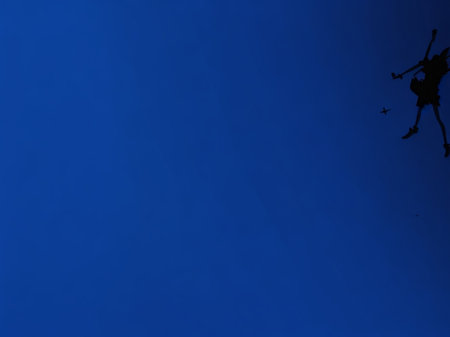 Silhouette of a man jumping on a blue sky background.の素材