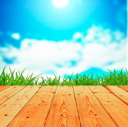 Fresh spring green grass with blue sky and wooden floorの写真素材