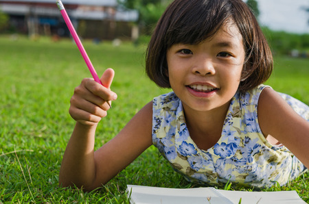 Cute little girl studying at school and smiling and green grassの写真素材