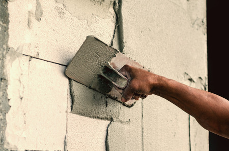 Construction worker holding plastering trowel smoothing wall defectsの写真素材