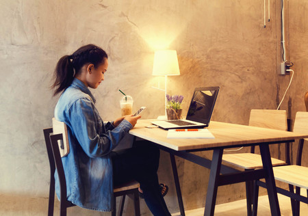 Beautiful young girl working at a coffee shop with laptop and coffee cup connecting internet,...