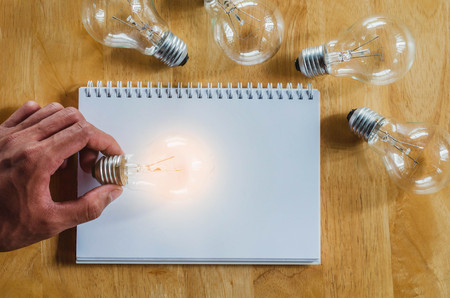 concept hand and light bulb isolate on notebook backgroundの写真素材