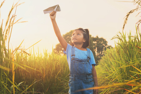 cute asian children playing paper airplane at rice field with sunset backgroundの写真素材