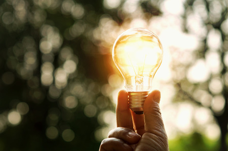 hand holding light bulb and sunset in nature, power energy conceptの写真素材