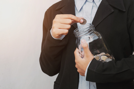 business hand putting coins in glass jar for saving money accounting conceptの写真素材