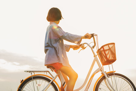 young asian woman riding bicycle at park with sunsetの写真素材