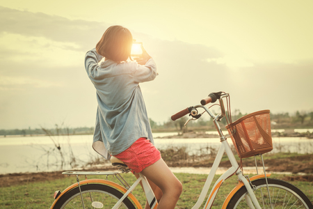 young asian woman on bicycle look at hand frame view sunsetの写真素材