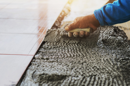 A close-up of a hand of a construction worker laying tile on the floor