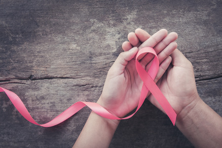hand holding pink ribbon on wood.  breast cancer awareness. concept healthcare and medicineの写真素材