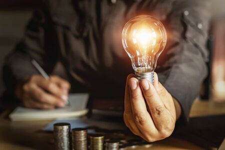 businessman holding light bulb with money stack.saving energy power conceptの写真素材