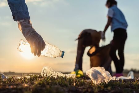 people volunteer keeping garbage plastic bottle into black bag at park river in sunsetの写真素材