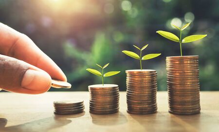 hand putting coins on stack with plant growing on money . finance and accounting concept