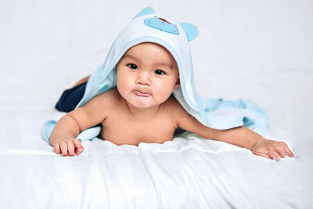 Baby boy wearing diaper with towel on white bed in bedroomの写真素材