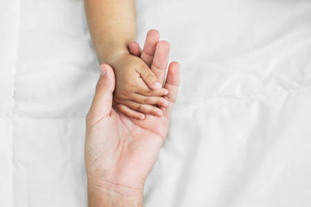 hand of mom and baby on white bedの写真素材