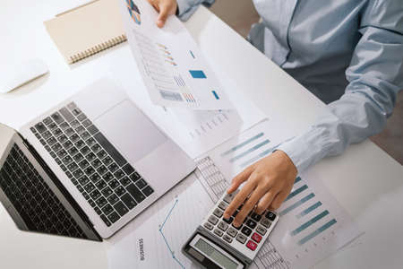 Woman accountant use calculator and computer with holding pen on desk in office. finance and accounting conceptの写真素材
