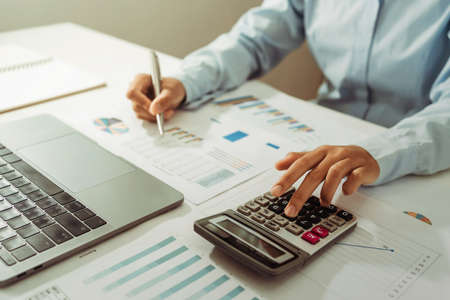 Woman accountant use calculator and computer with holding pen on desk in office. finance and accounting conceptの写真素材