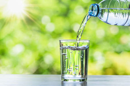 hand pouring water in bottle in to glass with sunshine on blur green backgoundの写真素材