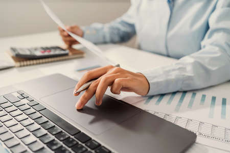 Woman accountant use calculator and computer with holding pen on desk in office. finance and accounting conceptの写真素材