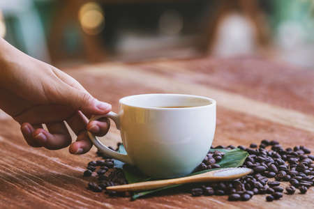 hand holding coffee cup with coffee beans on table and sunshine backgroundの写真素材
