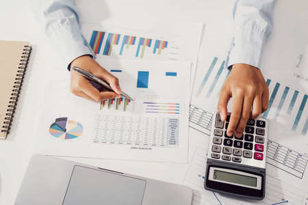 Woman accountant use calculator and computer with holding pen on desk in office. finance and accounting conceptの写真素材