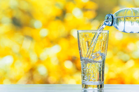 hand pouring water in bottle in to glass with sunshine on blur green backgoundの写真素材