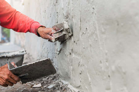 hand of worker plastering cement at wall for building house in construction siteの写真素材