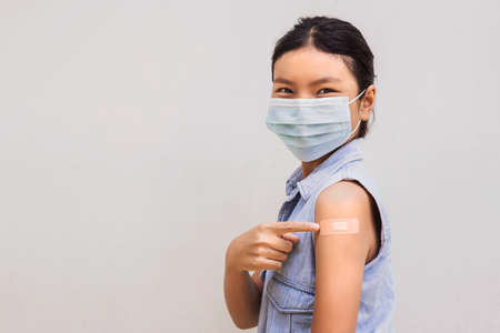 Portrait of a young female pointing plaster on arm after getting a vaccine. standing on white backgroundの写真素材