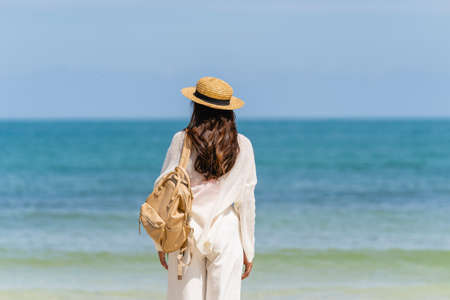 Woman wearing straw hat with bag standing on beach