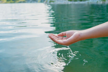 hand touches water in pond with sunshineの写真素材