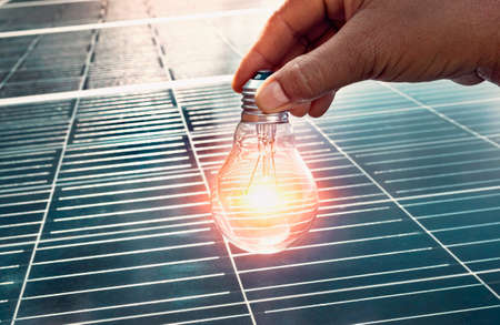 hand holding lightbulb on solar panel concept clean energy in natureの写真素材