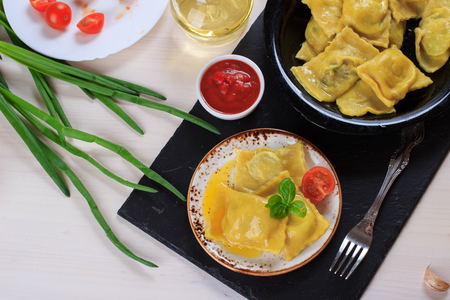 Traditional Italian homemade ravioli pasta stuffed with potatoes and spinach with tomato sauce, olive oil and basil on a black stone boardの写真素材