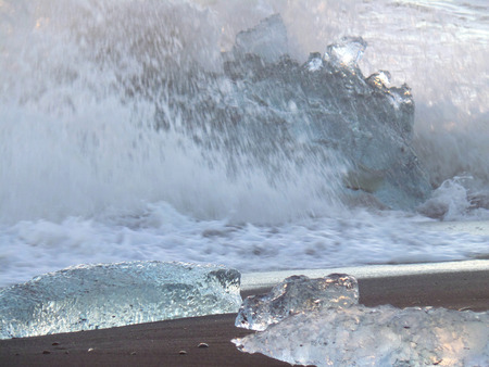 Powerful wave hitting huge icebergs on the black sand beach, South Iceland