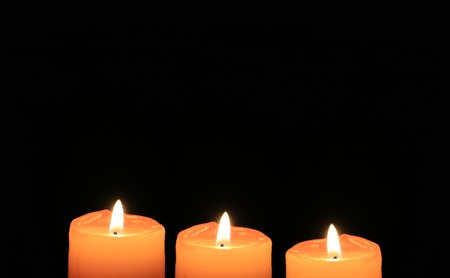 Three shining orange candles isolated on dark backgroundの写真素材