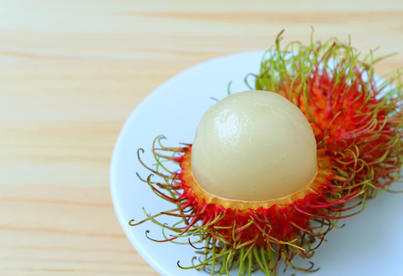 Close-up of Juicy White Fresh Ripe Rambutan Fruit on White Plate and Wooden Tableの写真素材