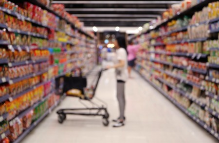Out of focus shot of a woman with her shopping cart in supermarket, looking at the grocery shelfの写真素材
