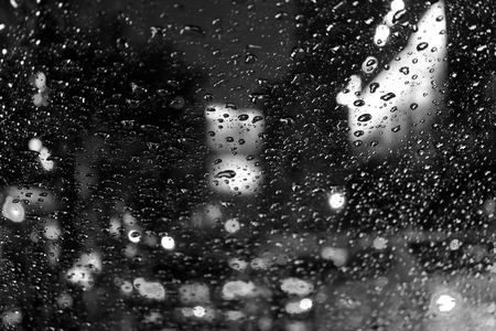 Monochrome photo of blurred street lights and tail lamps seen through raindrops on car windshield at nightの写真素材