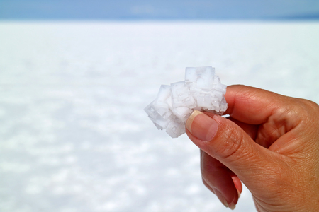Hand holding pure white natural salt crystals with blurred Salar de Uyuni Salt Flats of Bolivia in backgroundの写真素材