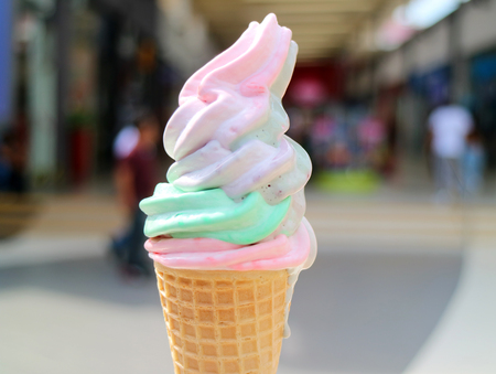 Melting Pastel Color Soft Serve Ice Cream Cone with Blurred Shopping Arcade in Backgroundの写真素材