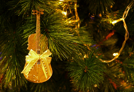 Shiny Gold Cello Shaped with Ribbon Bow Christmas Ornament Hanging on Sparkling Christmas Treeの写真素材