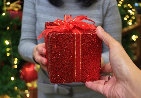 Closed up a hand of a man holding red square gift box handing to a womanの写真素材