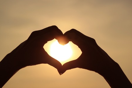 Silhouette of female's hand posing LOVE HEART sign against the shiny rising sunの写真素材