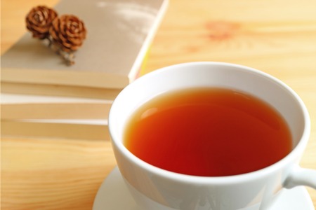 Closed up a cup of hot tea on wooden table with blurred stack of books and dry pine cones on top in backgroundの写真素材