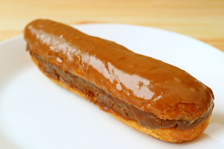 Close Up Mouthwatering Caramel Eclair Filled with Chocolate Served on White Plateの写真素材