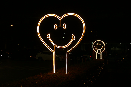 Heart shaped smiling face neon light sign on the street side at nightの写真素材