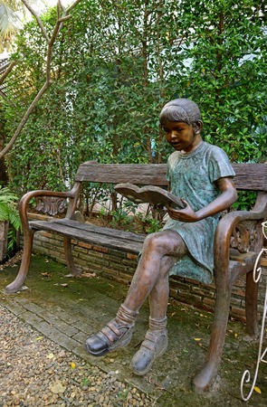 Bronze bench with a reading girl sculpture in the greenery gardenの写真素材